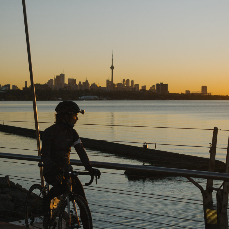 Cyclist watches Toronto skyline at sunset.